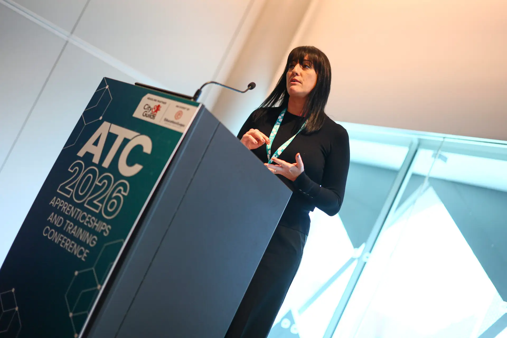 Female speaker at a podium delivering a talk at a conference, with a banner that reads ATC 2026 Apprenticeships and Training Conference