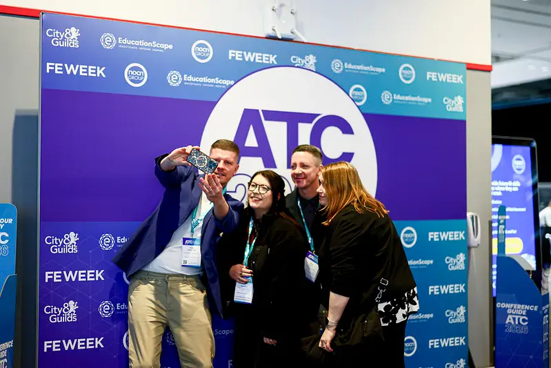 Four conference attendees pose for a selfie in front of an atc banner with fe week logos, wearing lanyards.